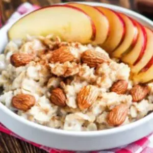 A bowl of oatmeal with almonds and sliced apples.