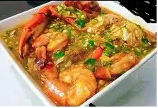 A bowl of shrimp and vegetables in sauce.